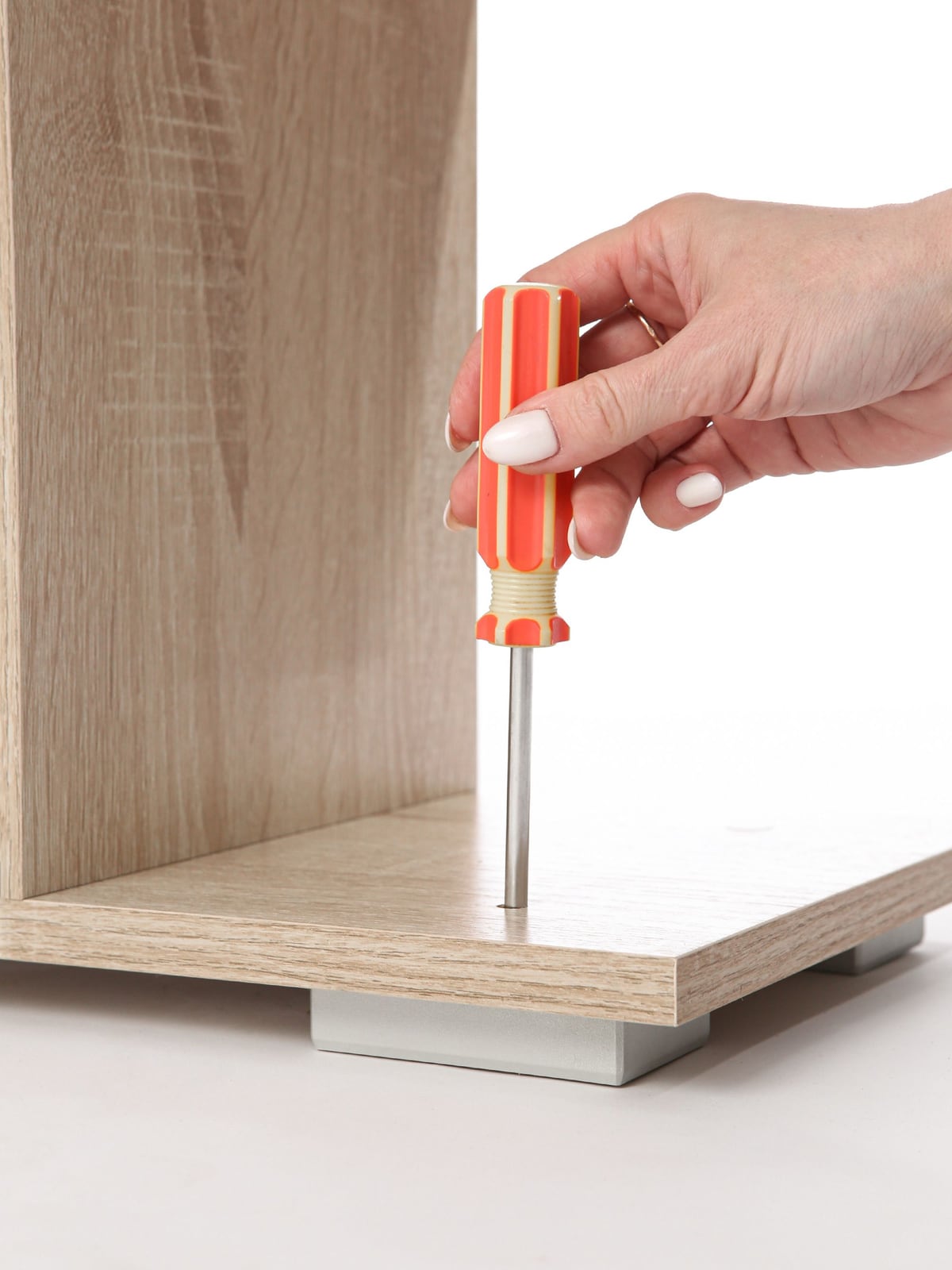 A hand tightening a screw in wooden furniture with a screwdriver