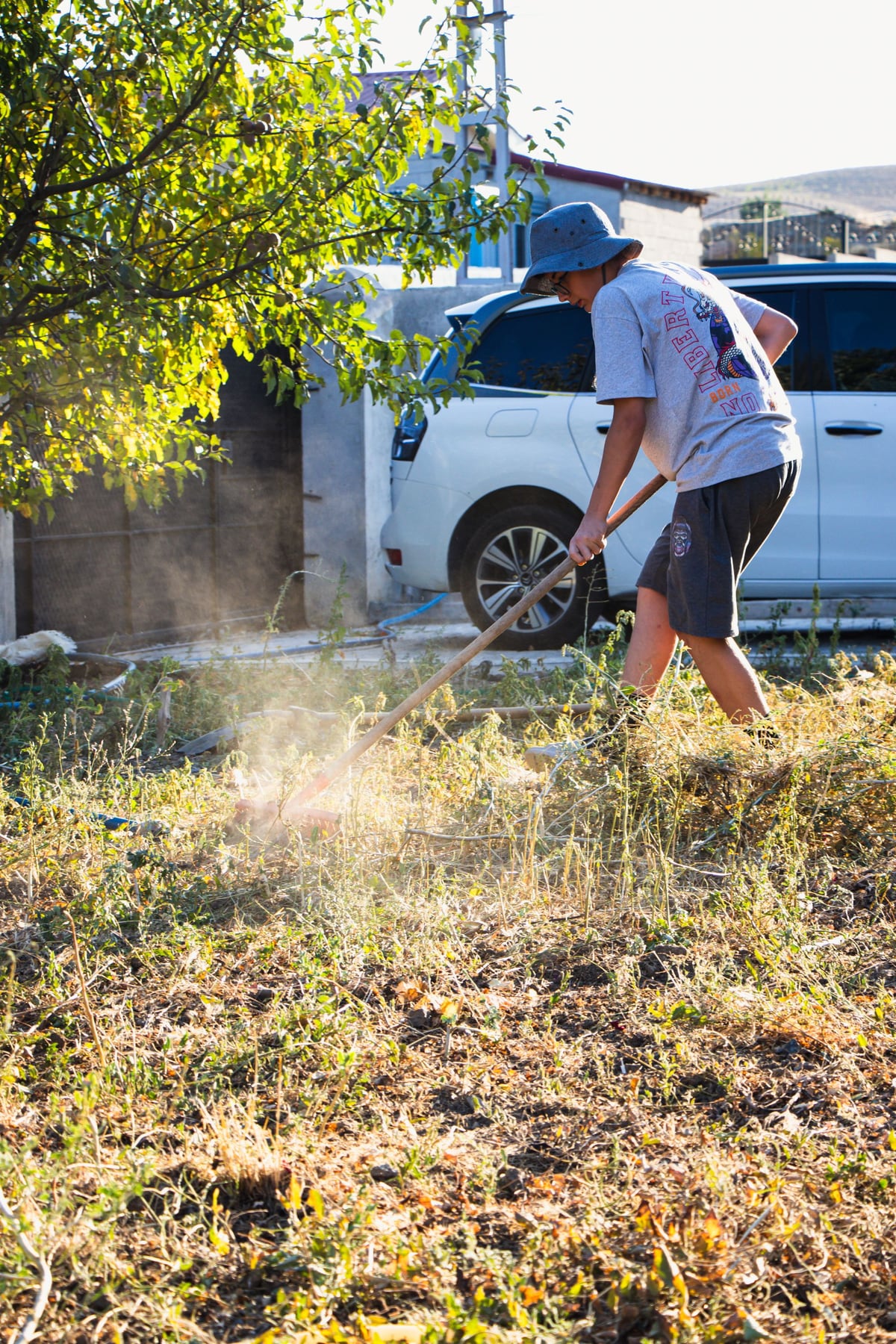 A person wearing a hat raking a yard in daylight